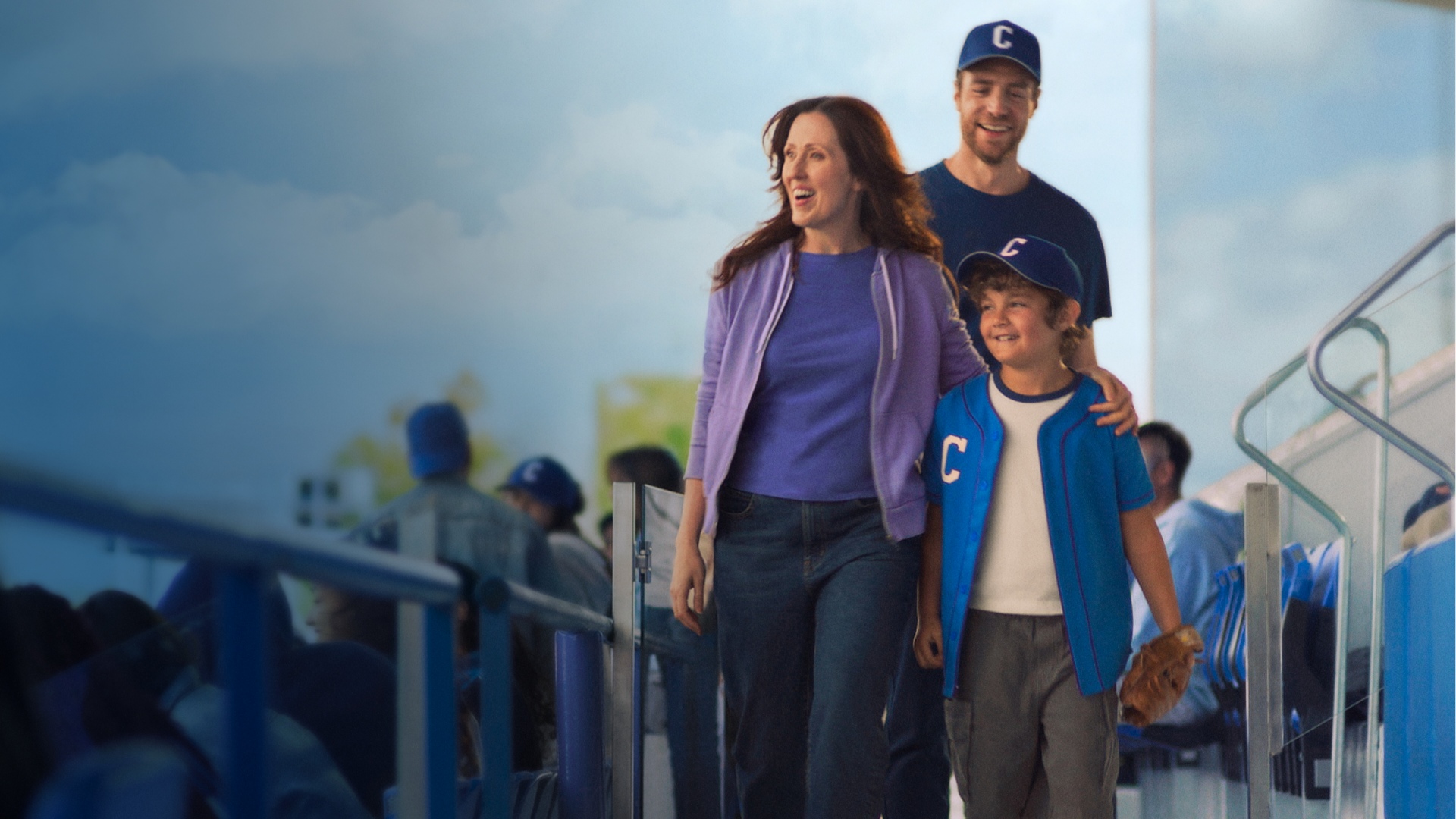 Actor portrayal of a CAMZYOS® (mavacamten) patient smiling and walking with a man and a young boy at a baseball stadium.