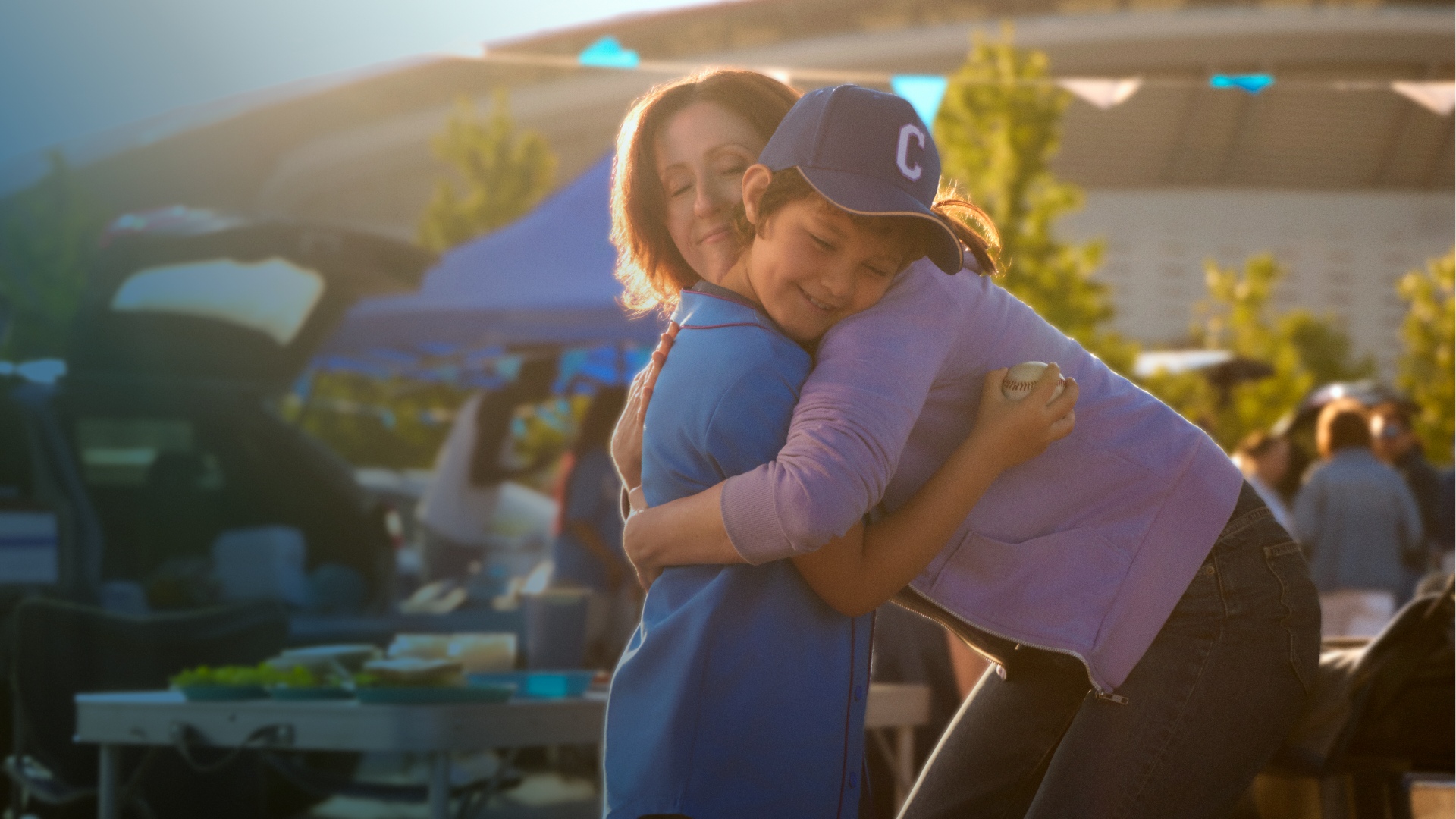 Actor portrayal of a CAMZYOS® (mavacamten) patient hugging a young boy outside of a baseball stadium.